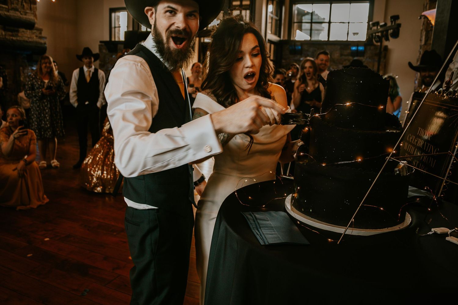 Bride and groom cutting a dark wedding cake together at their indoor wedding reception celebration.