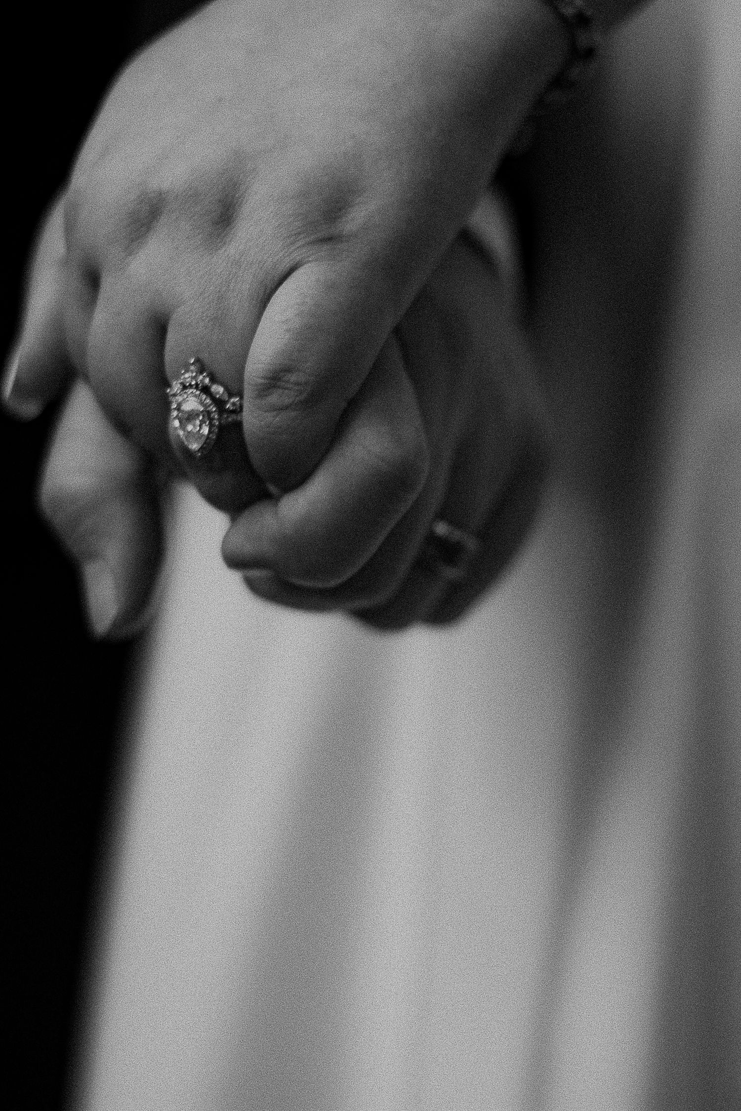 Black and white photo of two hands holding, featuring an elegant diamond engagement ring on the bride's finger.
