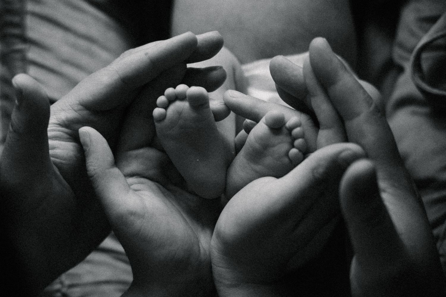 Black and white photo of newborn baby feet cradled gently in two adult hands.