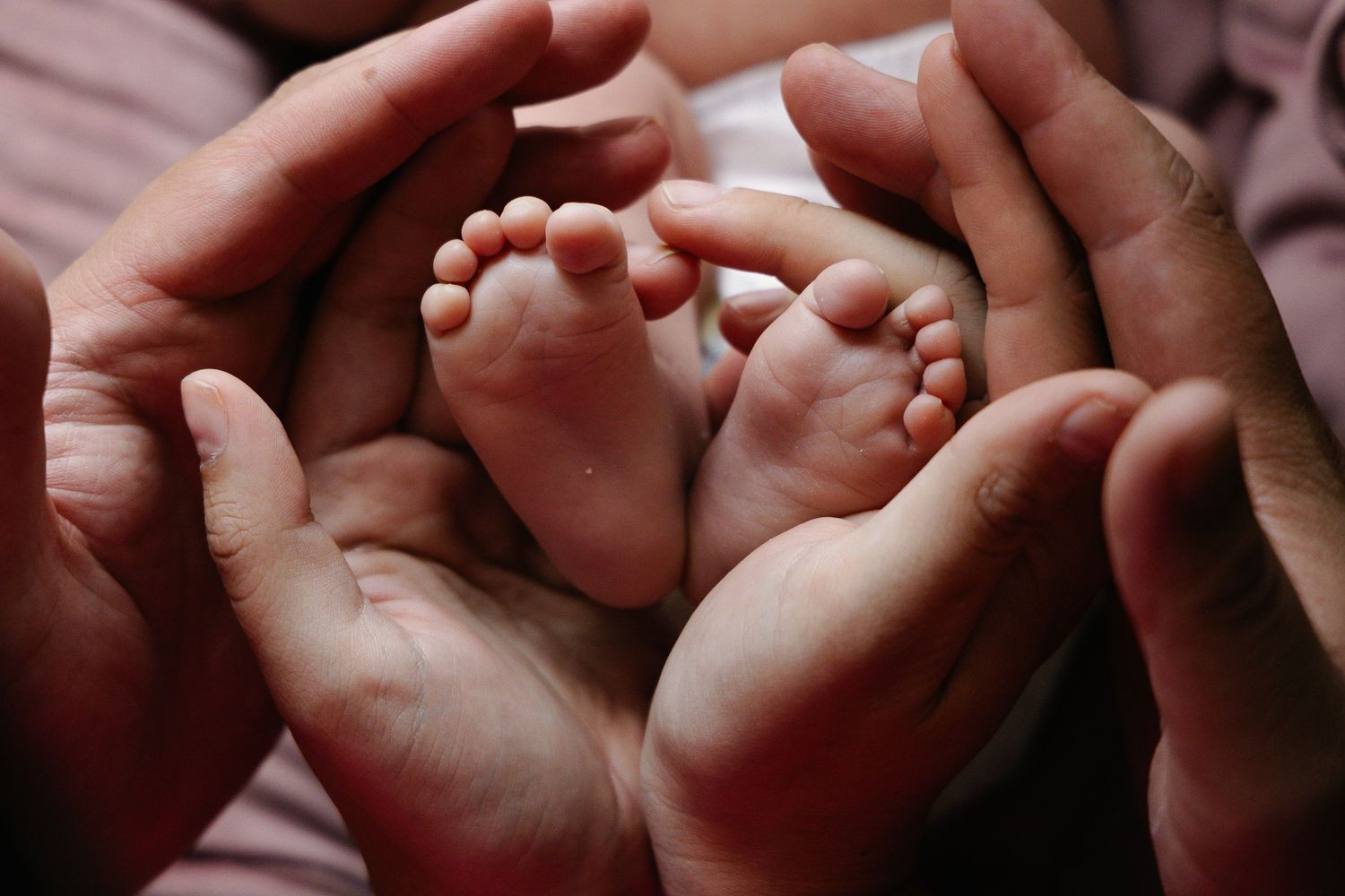 Adult hands cradling tiny newborn baby feet in a heart shape, symbolizing love and new parenthood.