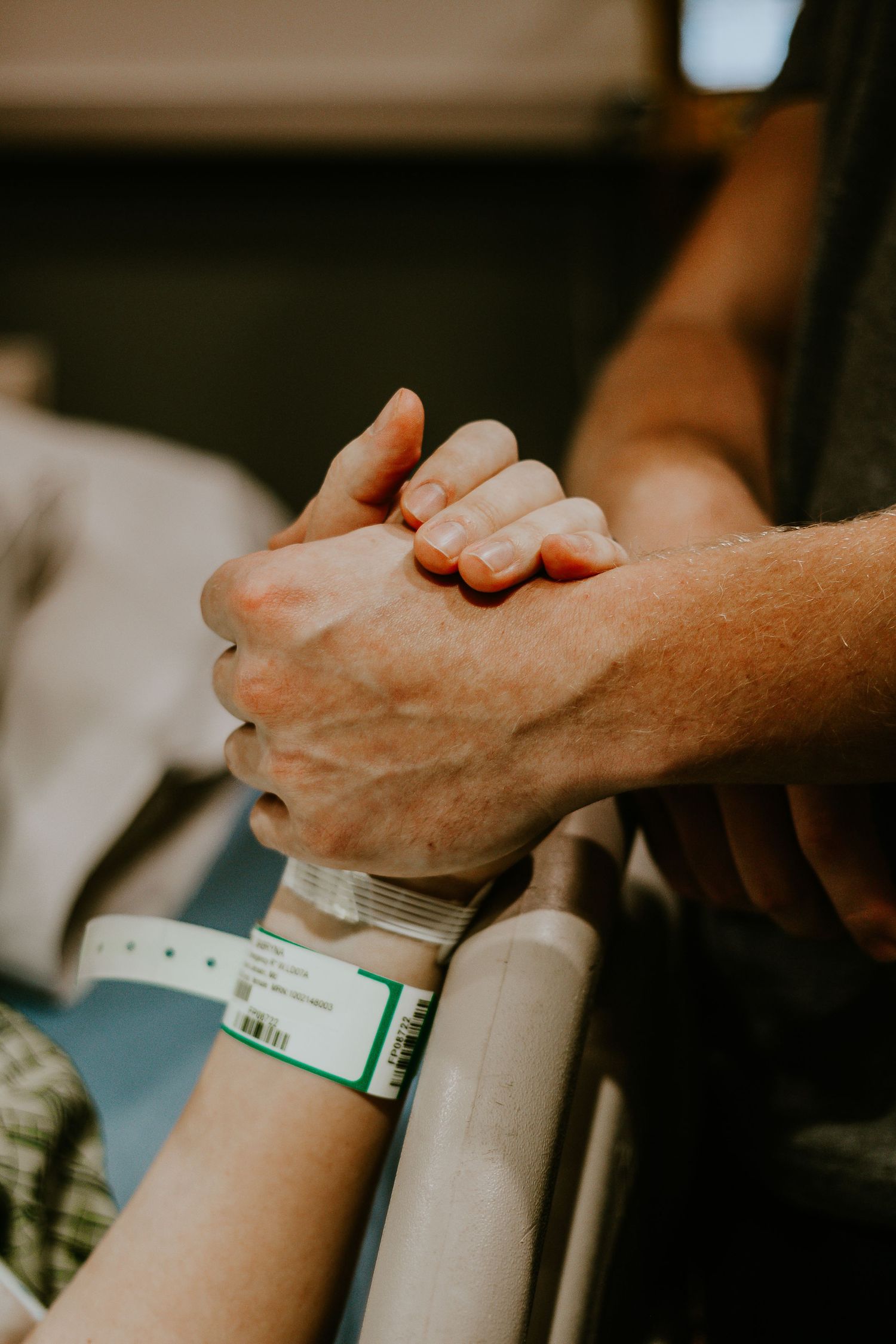 Two hands clasped together, one wearing a hospital ID wristband, sharing a comforting moment of support.