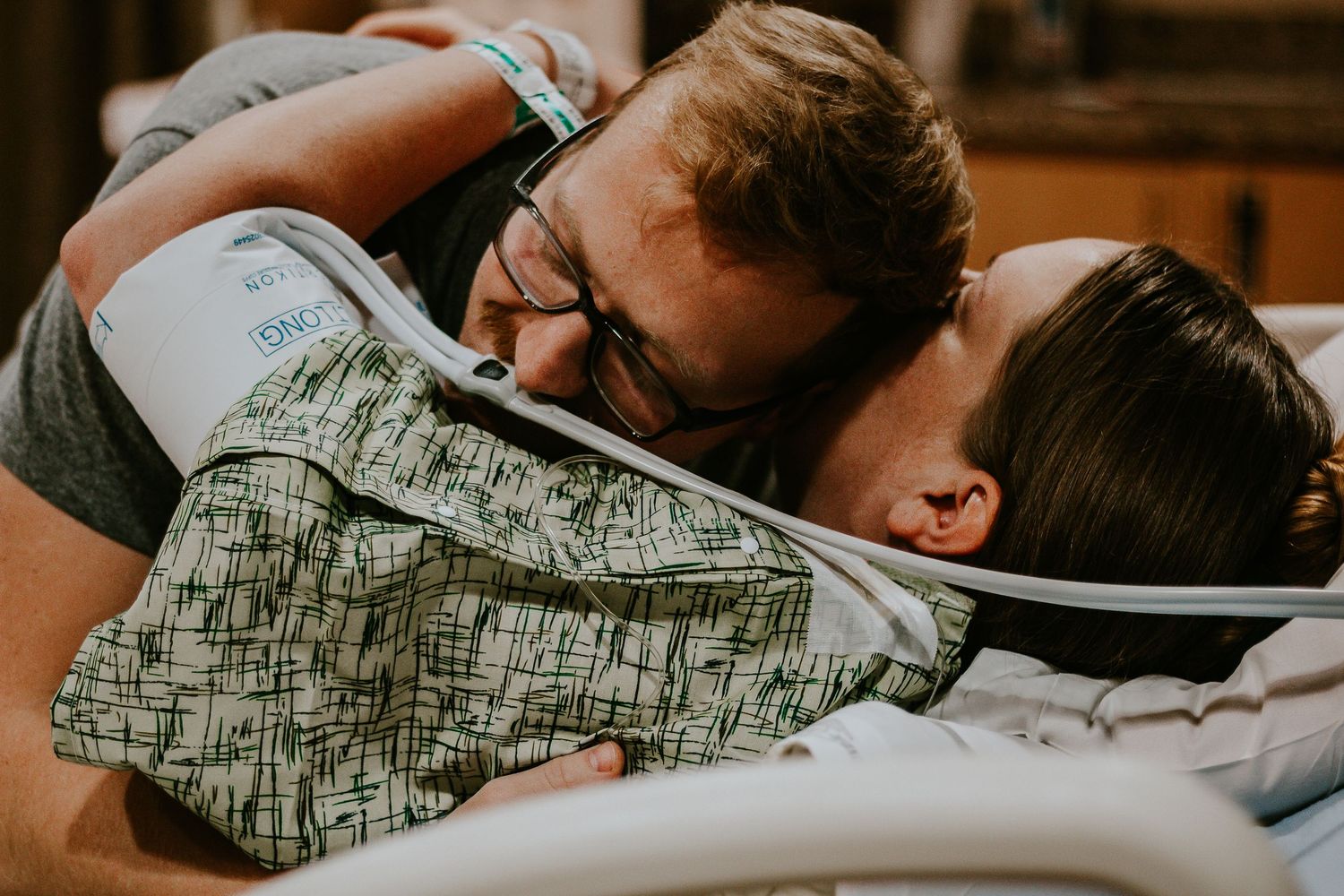 Emotional couple embracing in hospital bed, sharing tender moment after childbirth, wearing patient wristbands.
