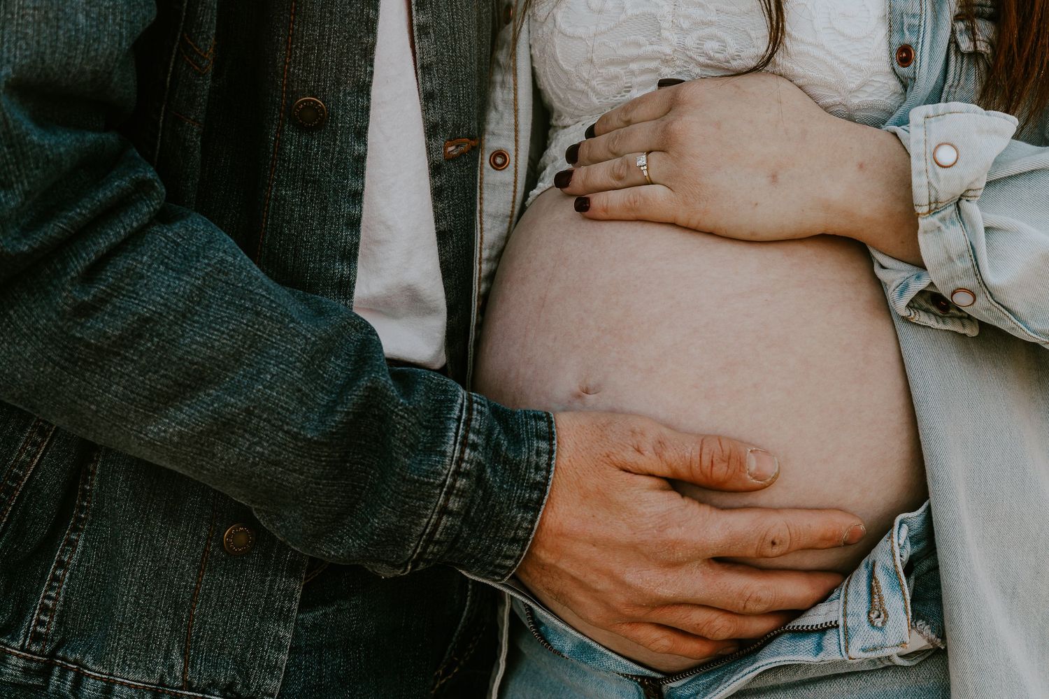 Couple cradling pregnant belly, wearing denim jackets, showcasing maternity love and pregnancy milestone.