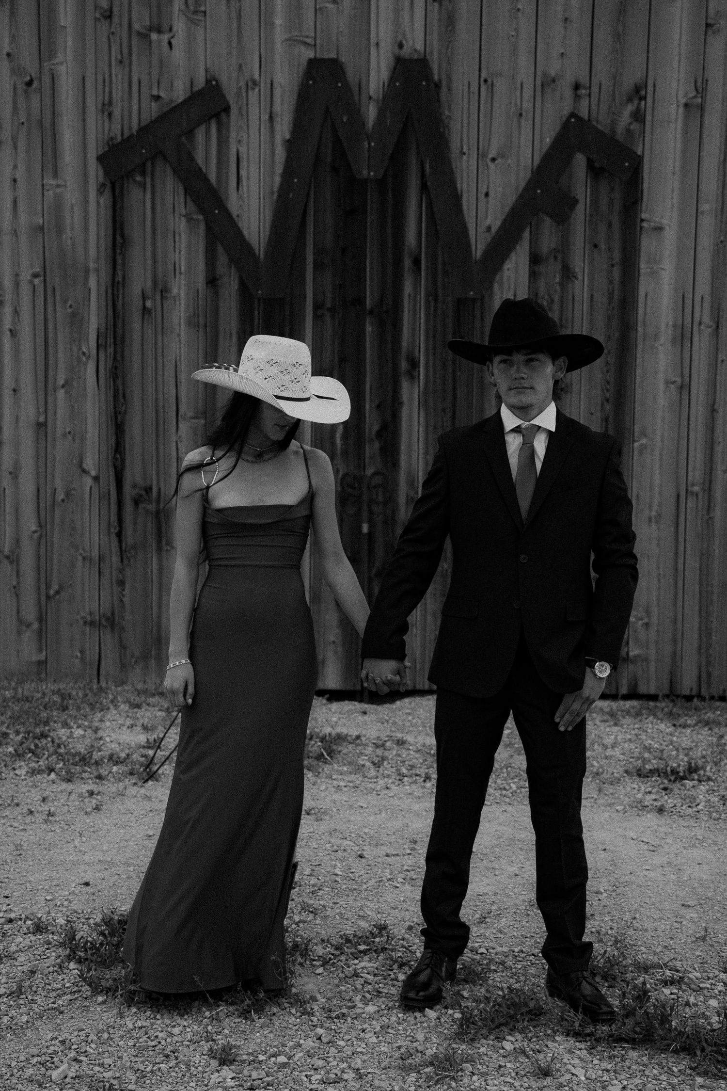 Black and white photo of a couple in western attire, woman in gown and white hat, man in suit and black cowboy hat.
