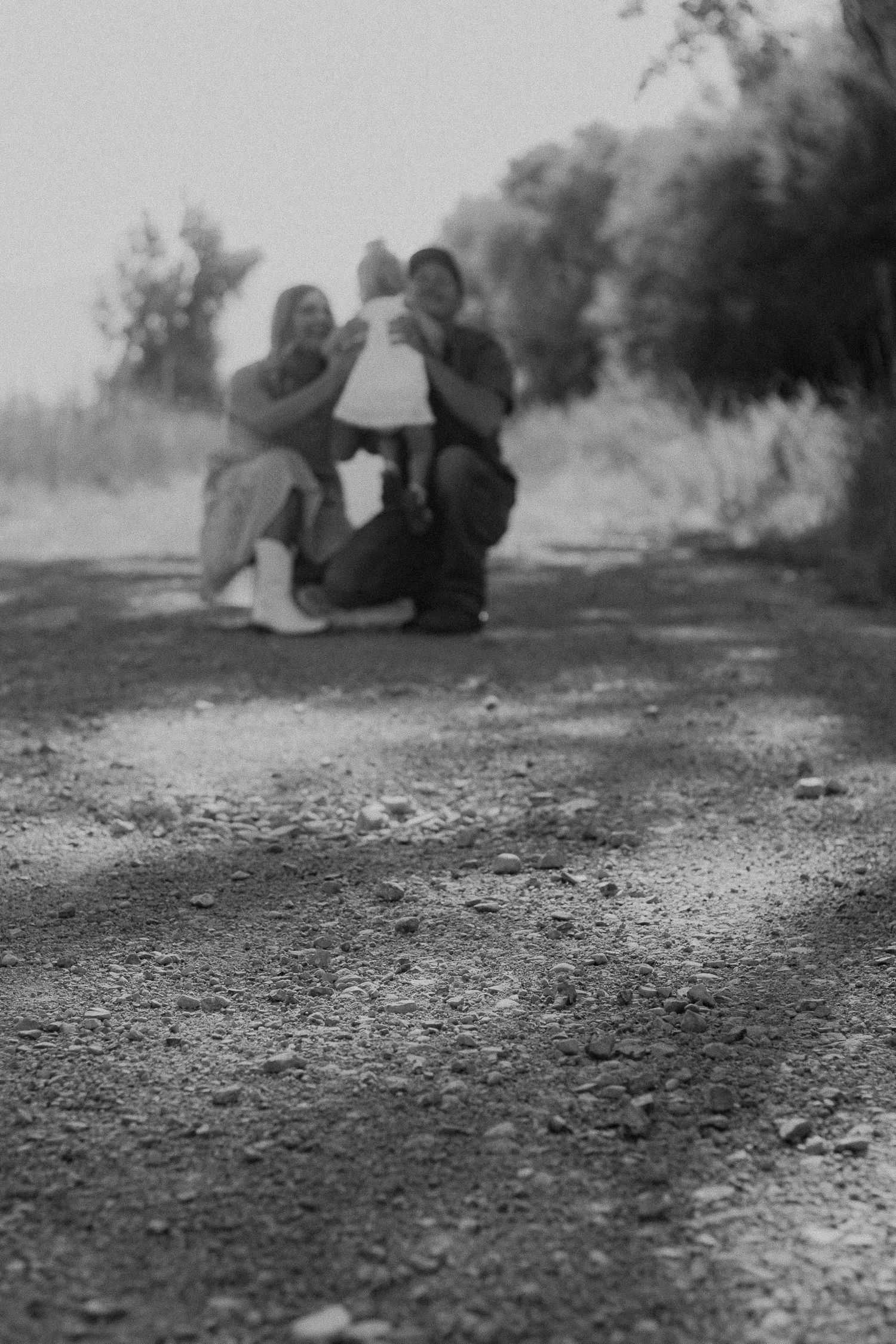 Black and white photo of a family posing together on a gravel path surrounded by trees.