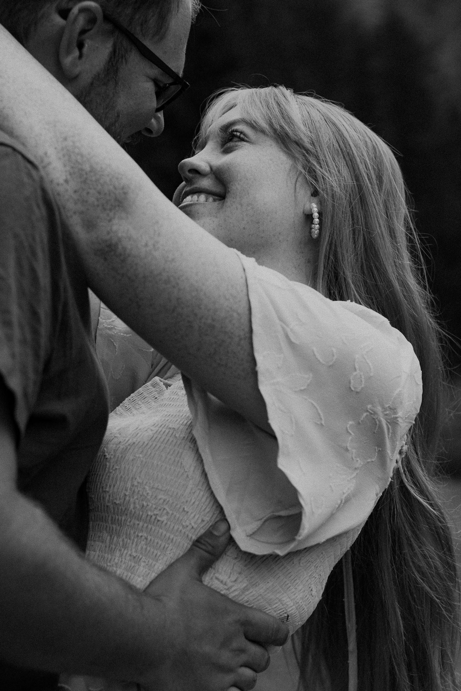 Black and white photo of a smiling woman gazing up at a man while they hold hands in a romantic outdoor setting.