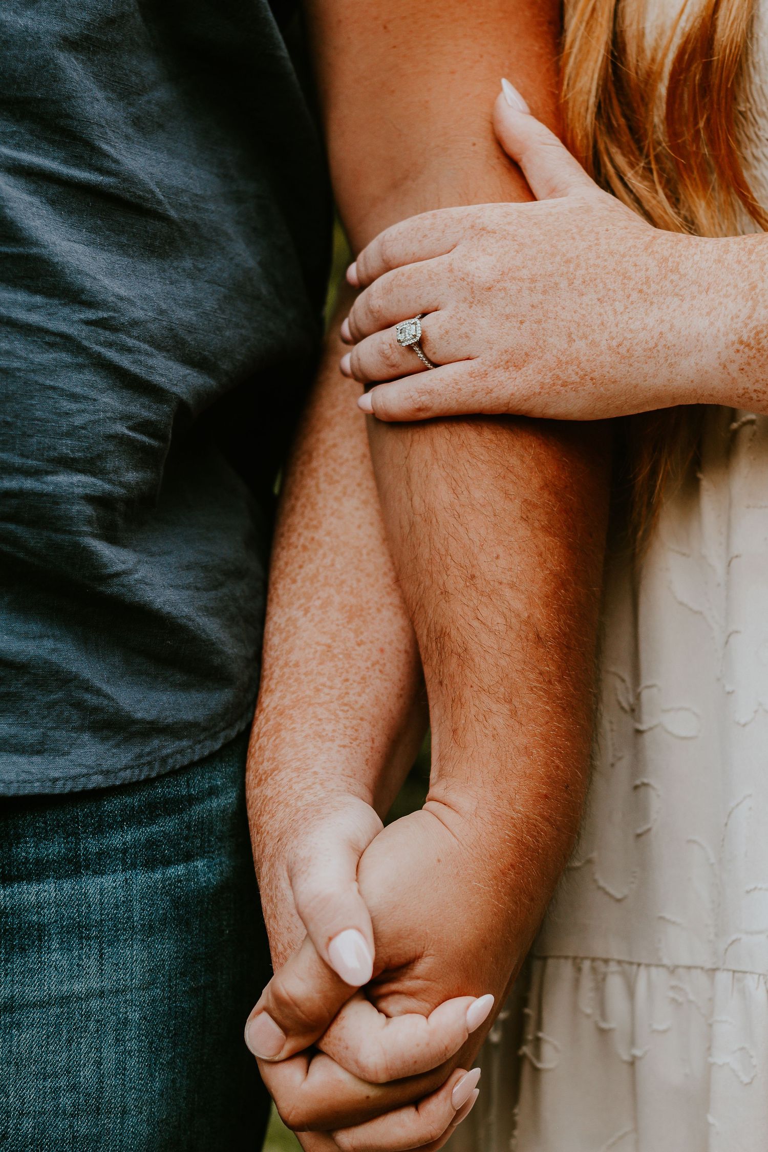 Couple holding hands with engagement ring visible, close-up romantic photo showing love and commitment.