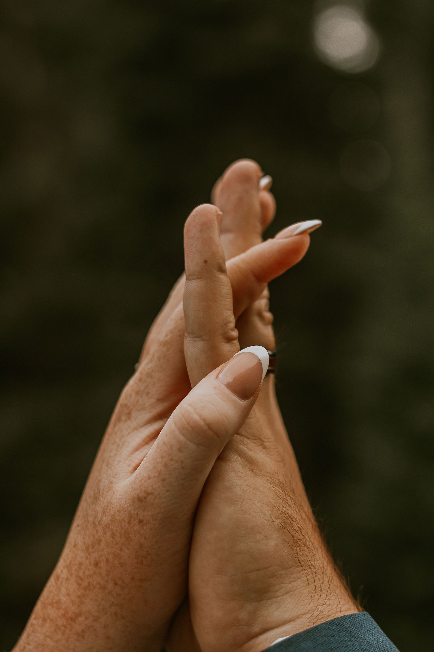 Two hands with French manicured nails gently touching against a blurred green background.