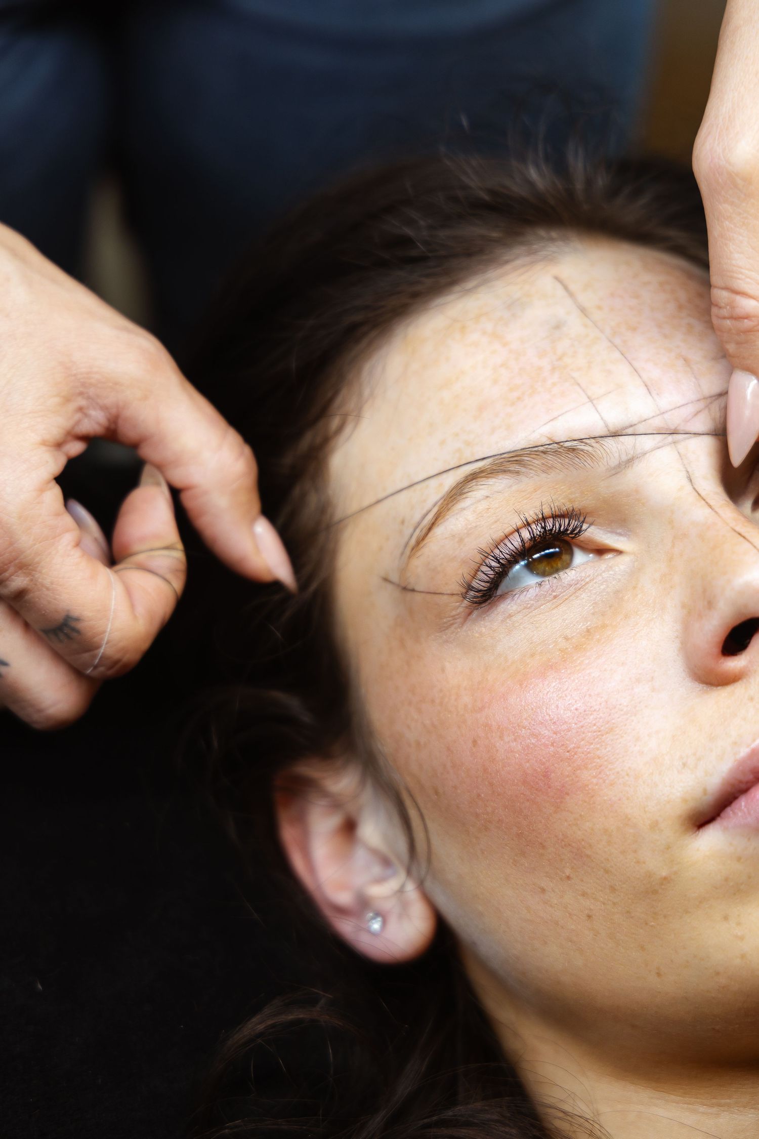Esthetician using thread to shape and define a young woman's eyebrows during a threading session.