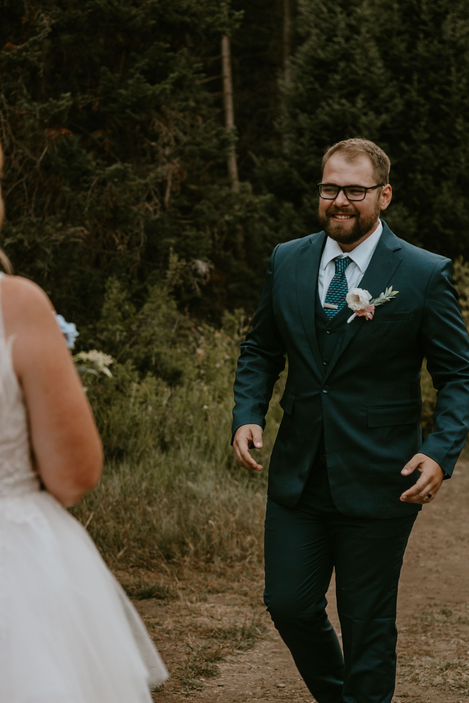 Groom in teal suit with boutonniere smiling at bride during outdoor forest wedding first look ceremony.