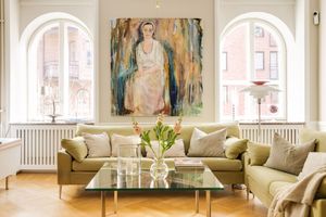 Modern living room with large arched windows, beige sofa, glass coffee table, and abstract artwork displayed on white walls.