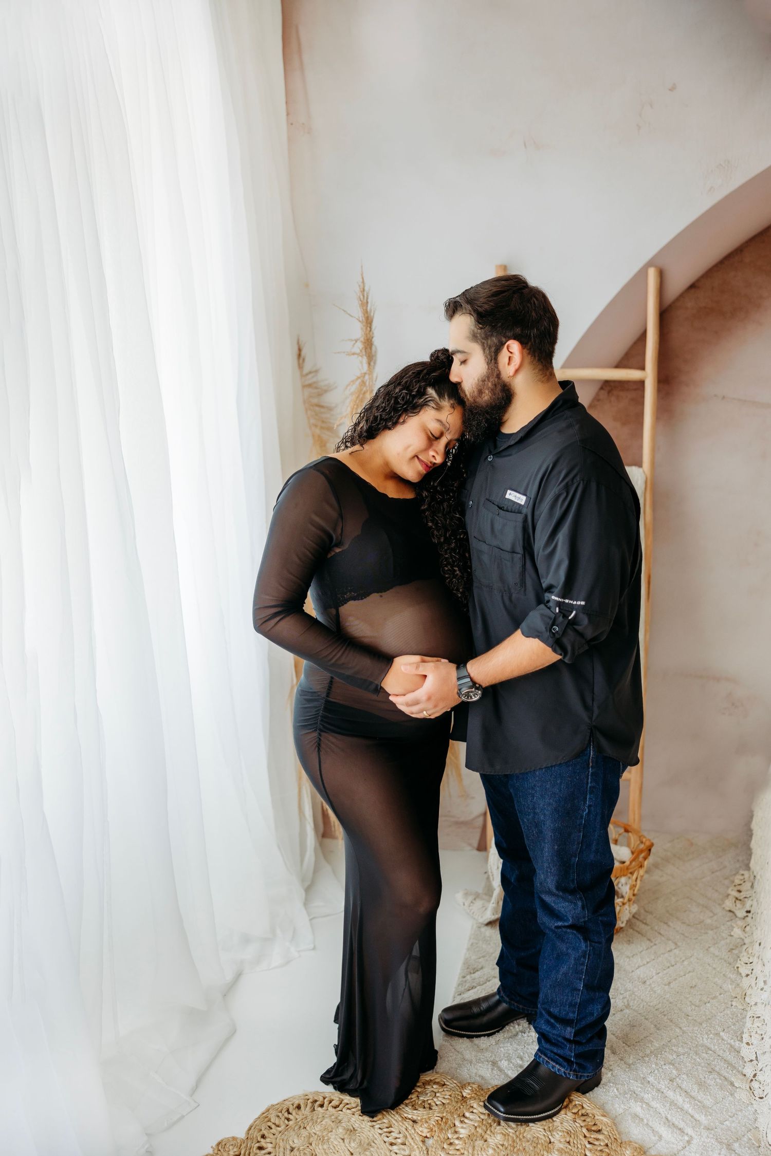 A couple in black and denim share intimate maternity poses against a white curtained backdrop in a photo series. Middle TN Maternity