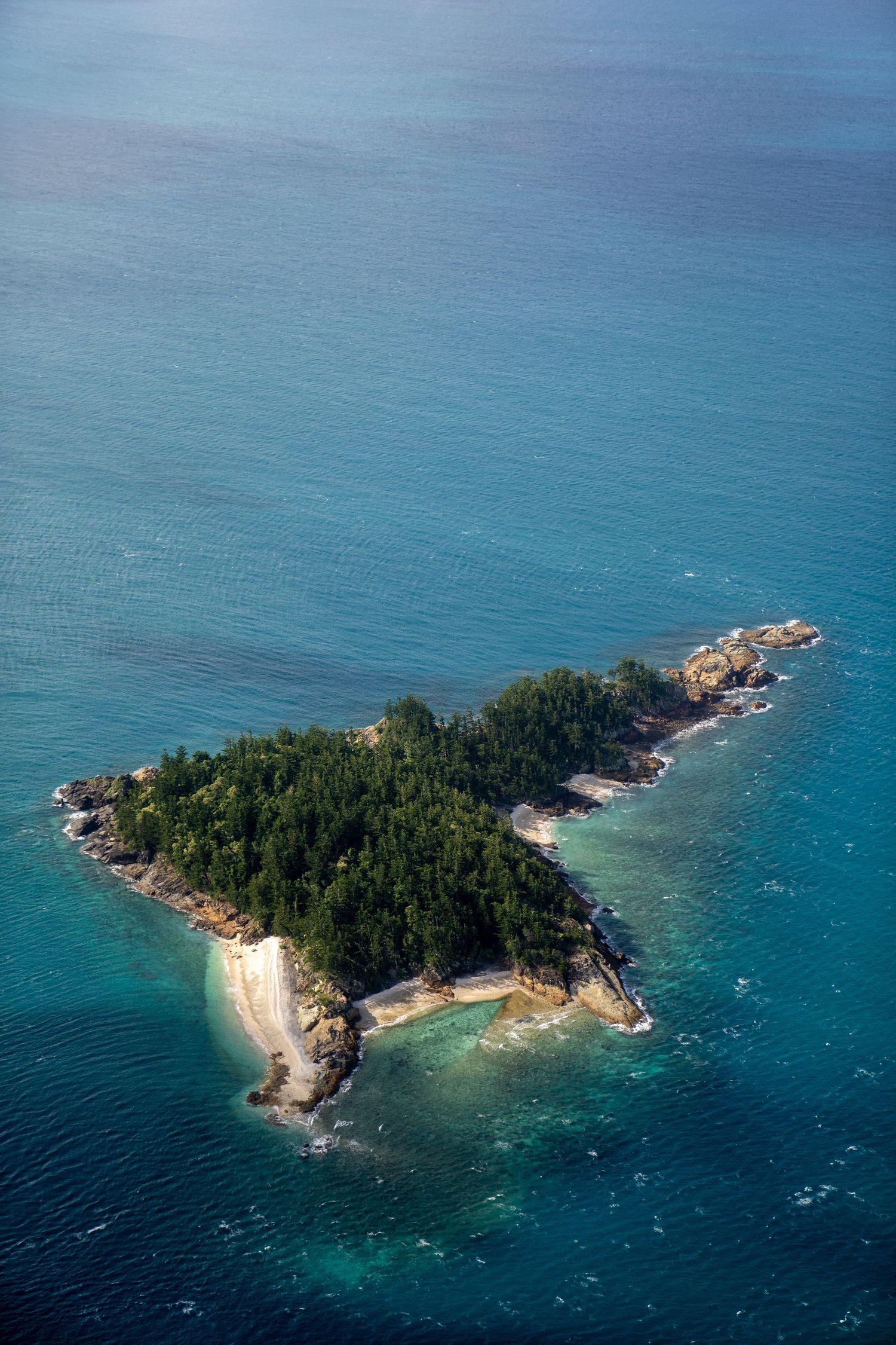 Aerial view of a small tropical island with white sandy beaches surrounded by crystal clear turquoise waters.