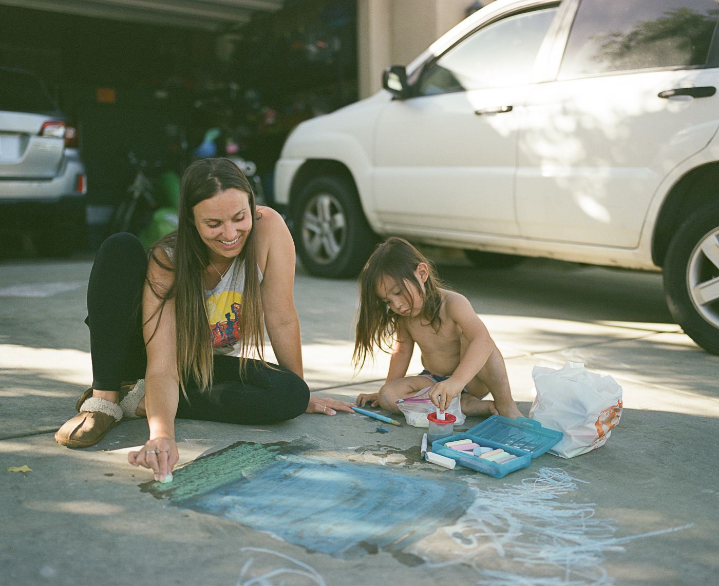 People working on a large chalk art drawing on a residential driveway.