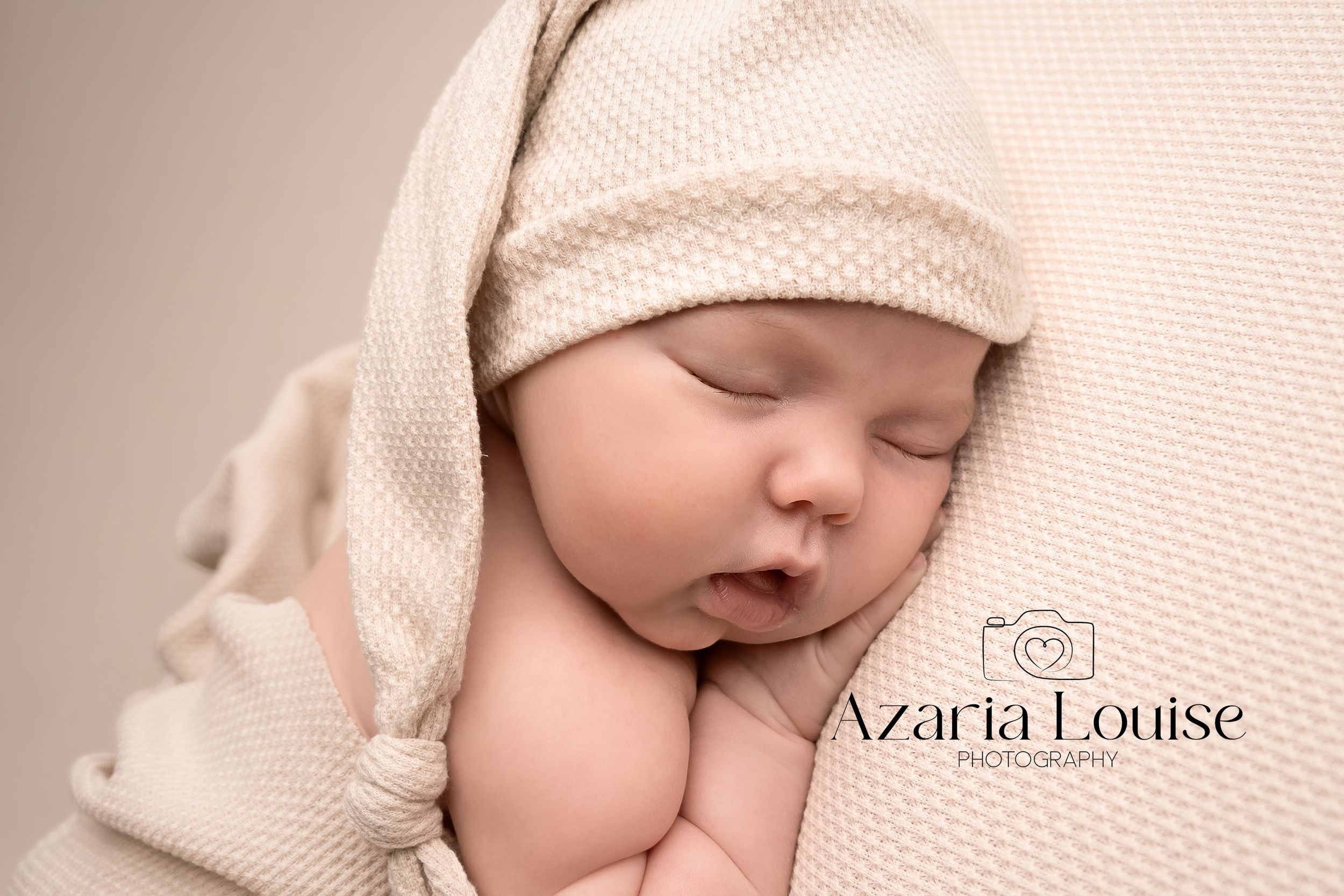 Sleeping newborn wrapped in beige knit blanket during professional portrait photography session.