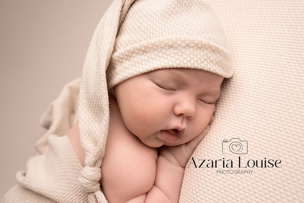 Sleeping newborn wrapped in beige knit blanket during professional portrait photography session.