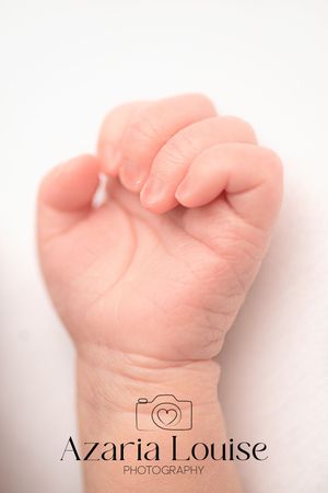 Close-up photograph of a tiny clenched baby fist against a white background.