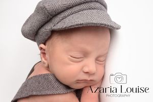Sleeping newborn baby wearing a gray herringbone newsboy cap in a studio portrait.