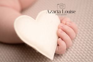 Tiny newborn baby toes next to a soft white felt heart on textured gray fabric.
