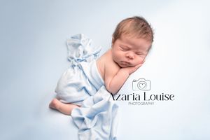 Sleeping newborn wrapped in soft blue fabric against light background for professional portrait photography.