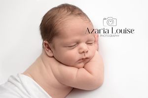 Peaceful sleeping newborn baby nestled against white backdrop in professional portrait setting.