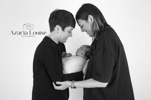 Black and white studio portrait of adults tenderly holding a newborn baby together.