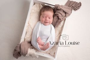Sleeping newborn baby wrapped in white swaddle lying in rustic wooden box with beige fabric.
