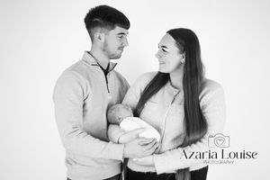 Black and white portrait of couple standing close together holding a sleeping baby.
