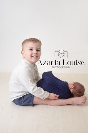 Two children posing on light wooden floor in studio setting with photography business logo visible.