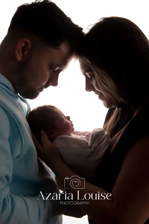A silhouetted couple lovingly gazes at their newborn baby against bright backlit window.