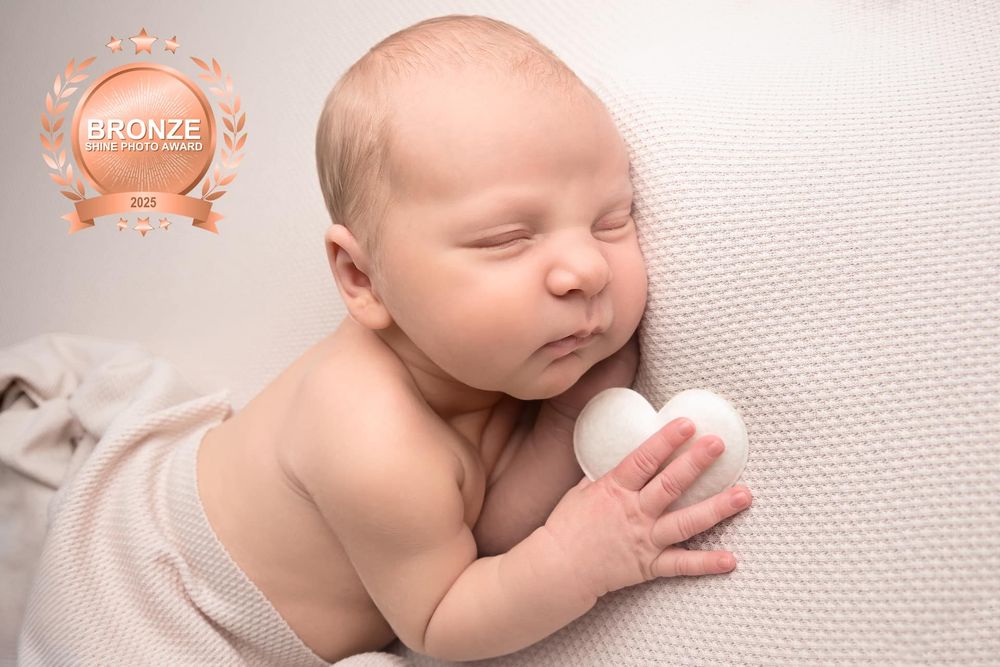 A peaceful sleeping newborn baby rests on soft white fabric while gently holding a small white ball.