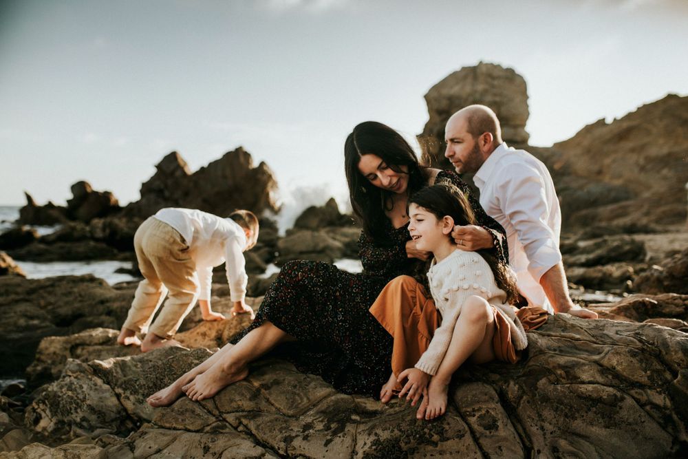 Family enjoying quality time together on rocky coastal cliffs during golden hour.