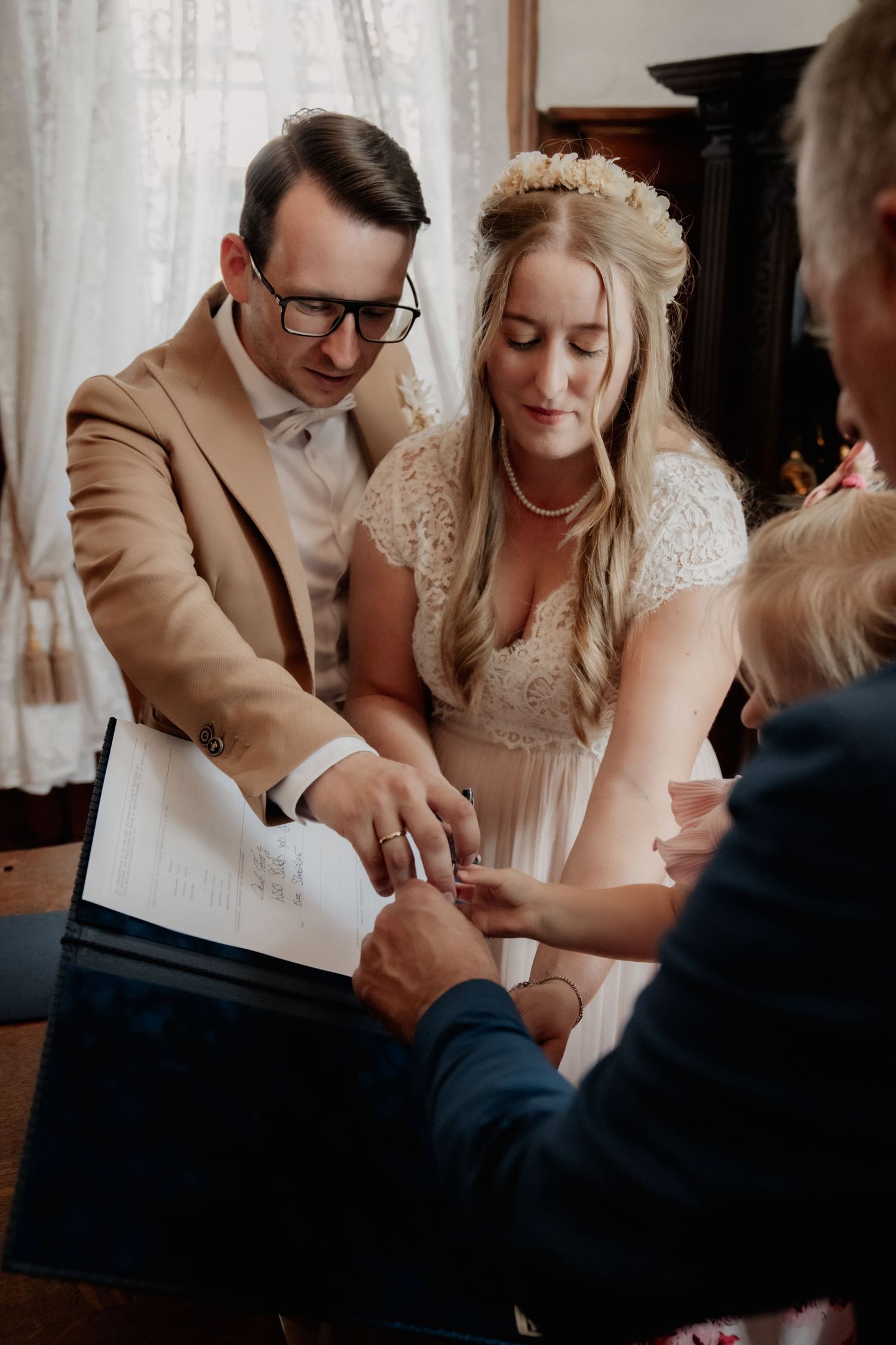 Couple in wedding attire signing documents at indoor ceremony.