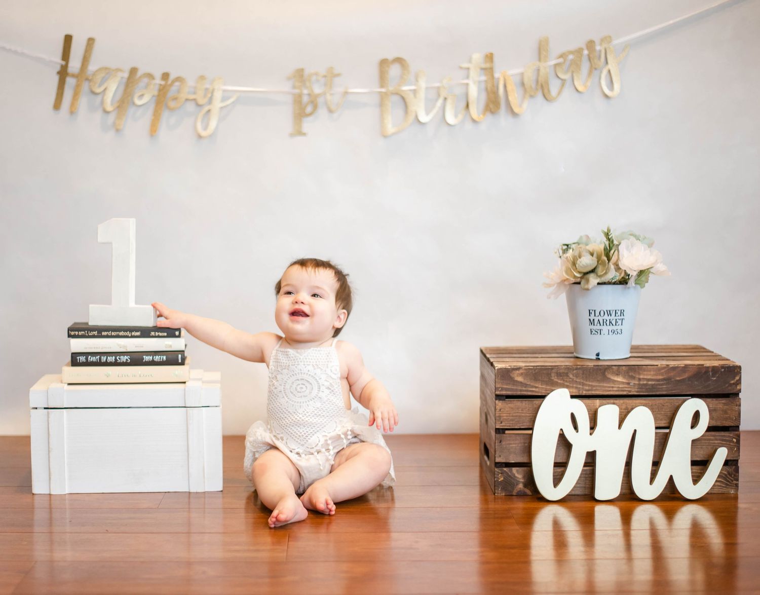 Baby on hardwood floor with rustic decorations and 'ONE' text display.
