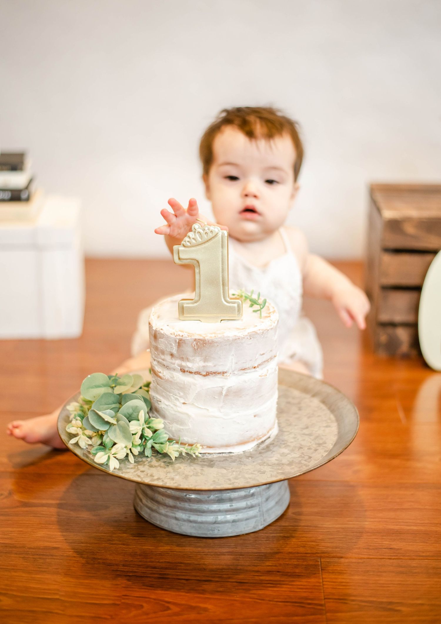 First birthday cake setup with baby on hardwood floor during celebration photoshoot.