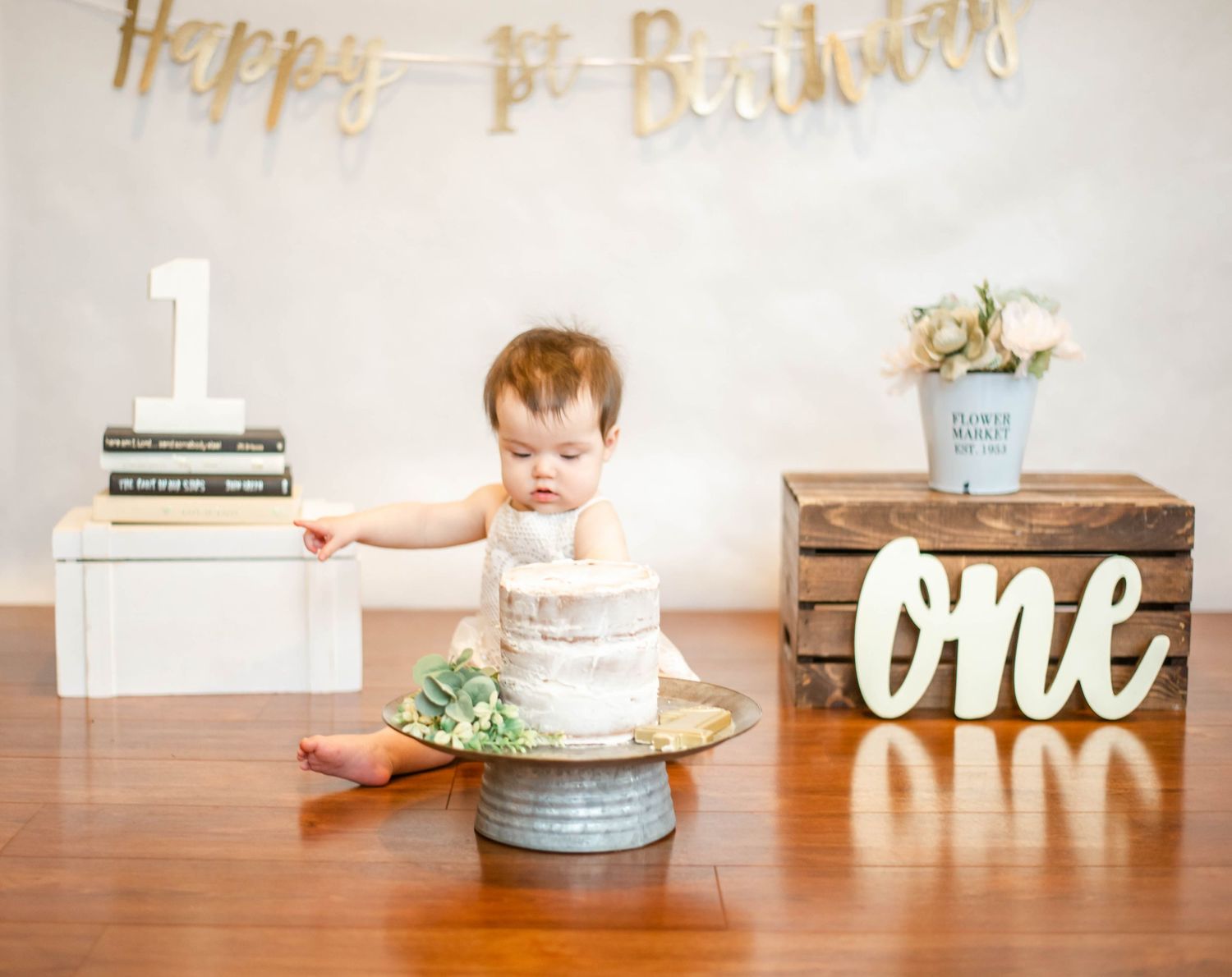 First birthday celebration display featuring a white cake and gold lettering decorations.
