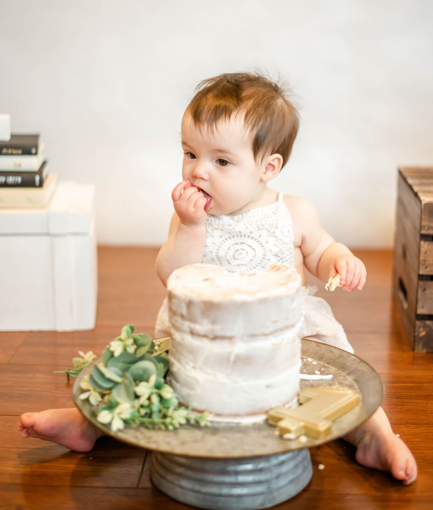 Toddler explores elegant white wedding cake with eucalyptus decorations on vintage cake stand.