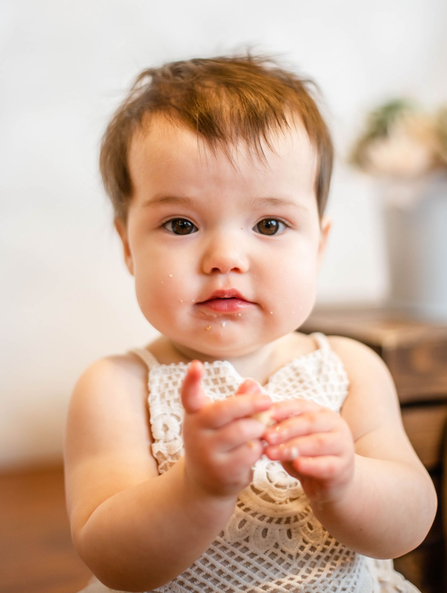Small child in polka dot outfit eagerly reaches for cake during first birthday celebration.