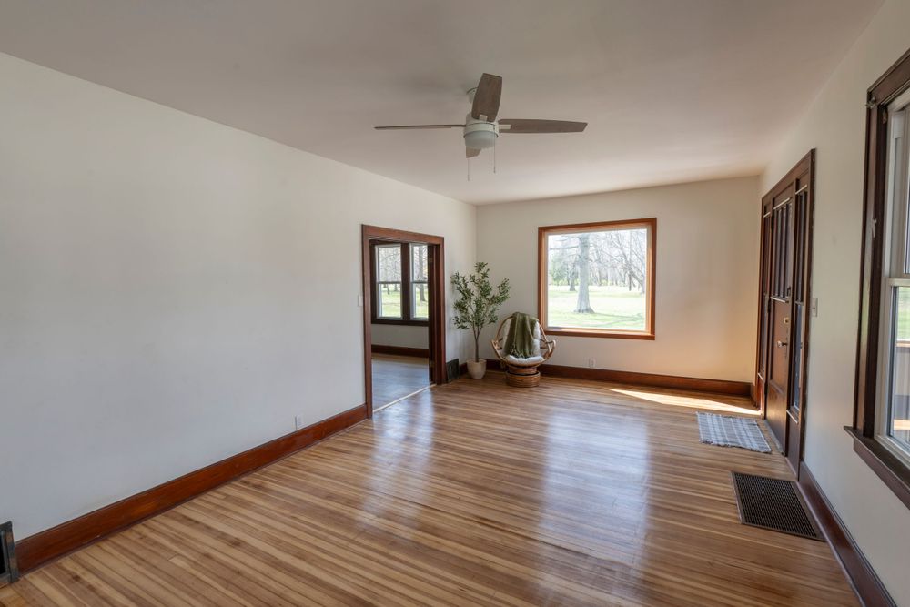 Empty room with hardwood floors, white walls, and natural light streaming through windows.