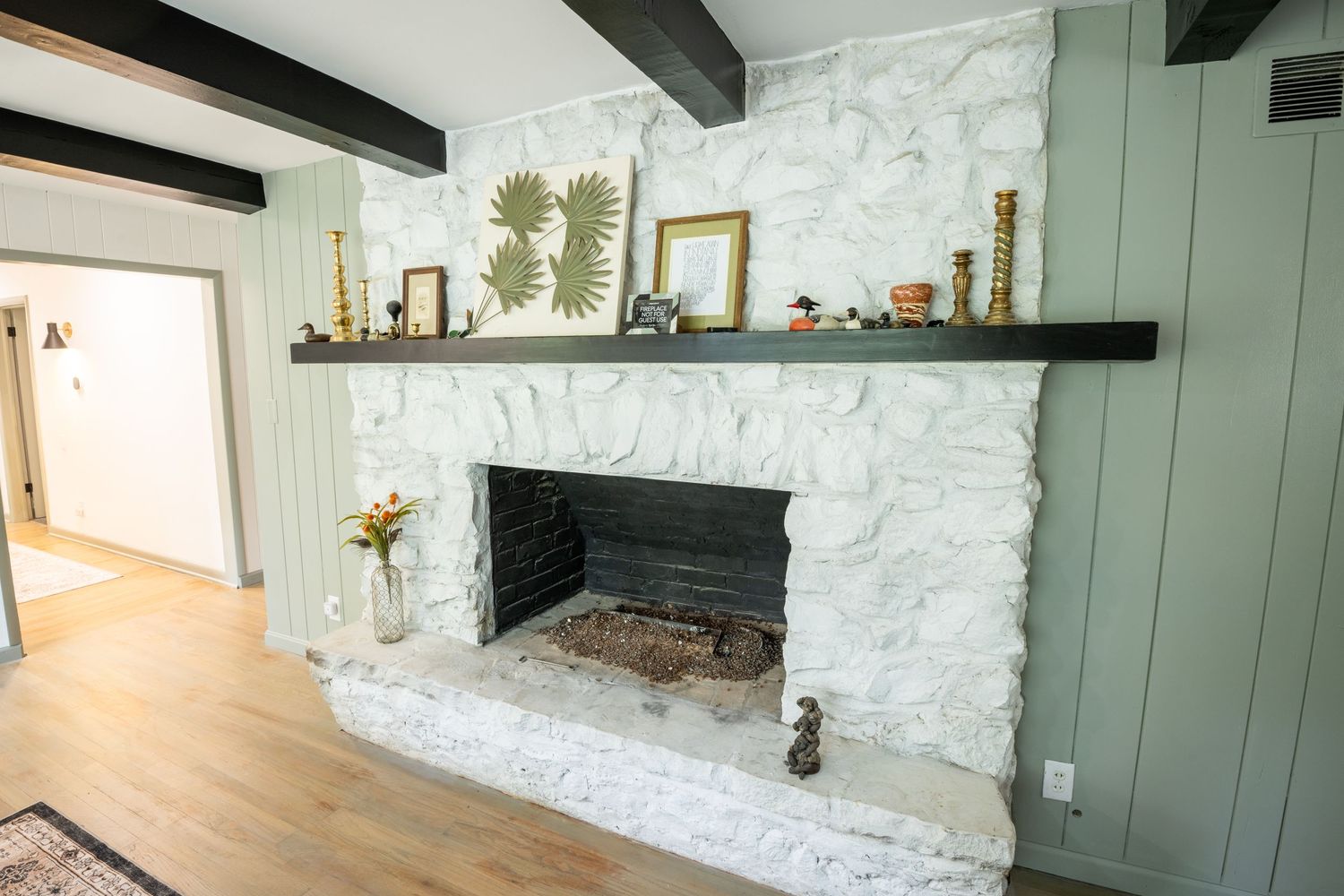 Painted white stone fireplace with dark wood mantle shelf and hardwood floors.