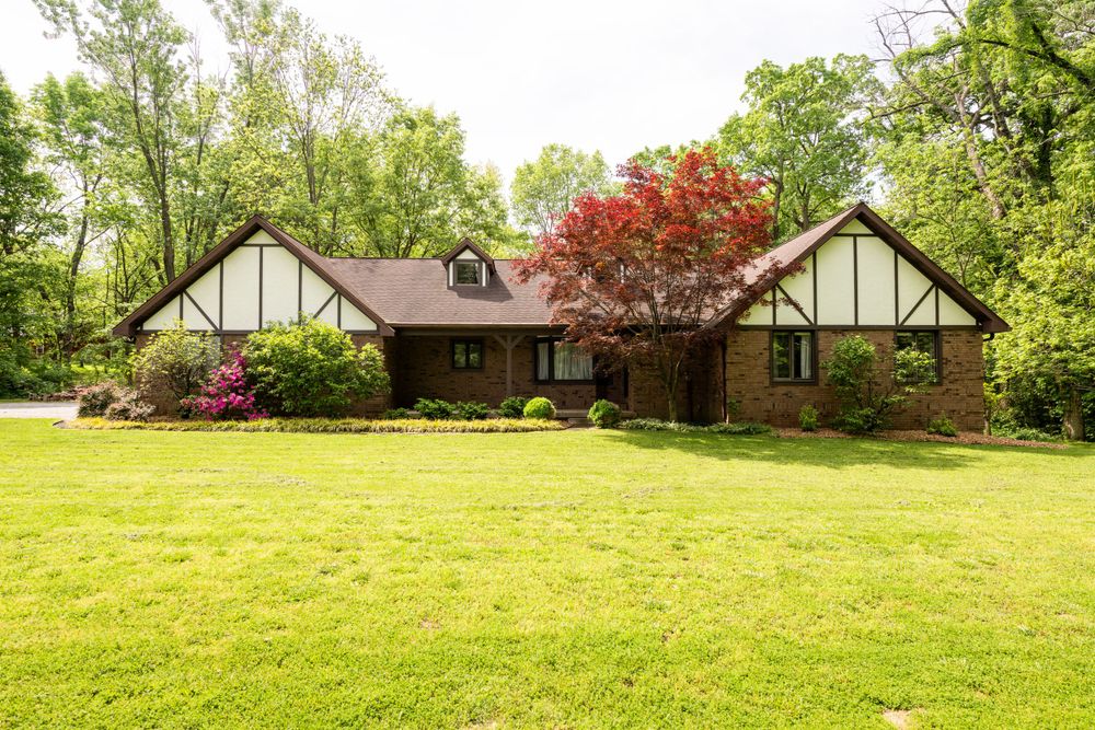 Tudor style brick home with red maple tree and manicured lawn in springtime.