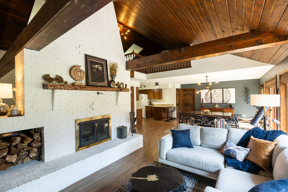 Rustic living space with white stone fireplace, wood ceiling beams and comfortable seating area.