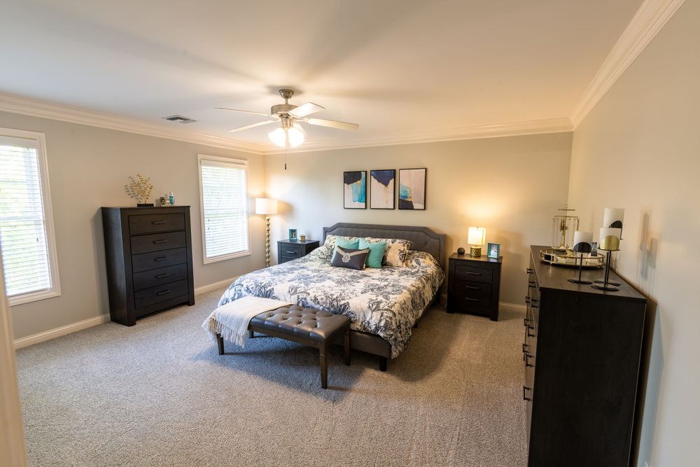 Spacious master bedroom with black furniture, ceiling fan and floral bedding.