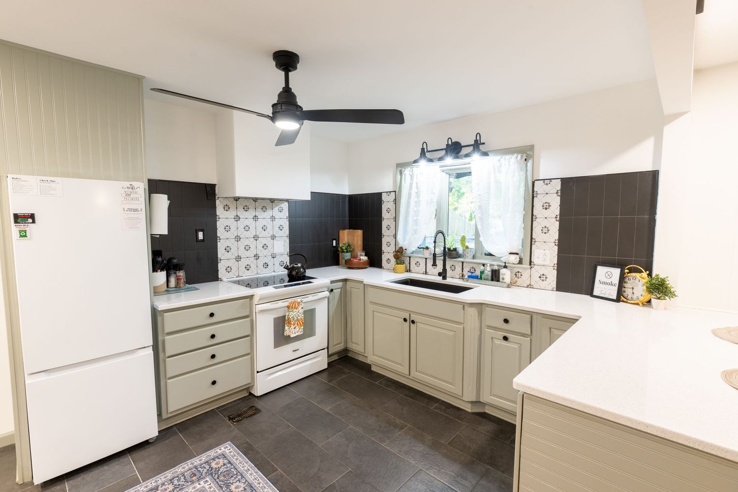 Modern L-shaped kitchen with light beige cabinets, white appliances, dark tile floors and a ceiling fan.