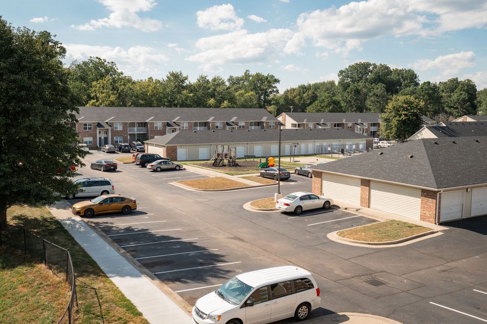 Aerial view of a residential apartment complex with white buildings and paved parking areas under a partly cloudy sky.