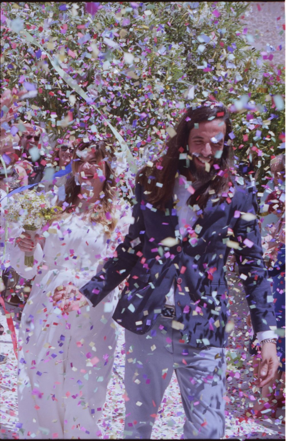 Couple celebrating under shower of colorful confetti outdoors.