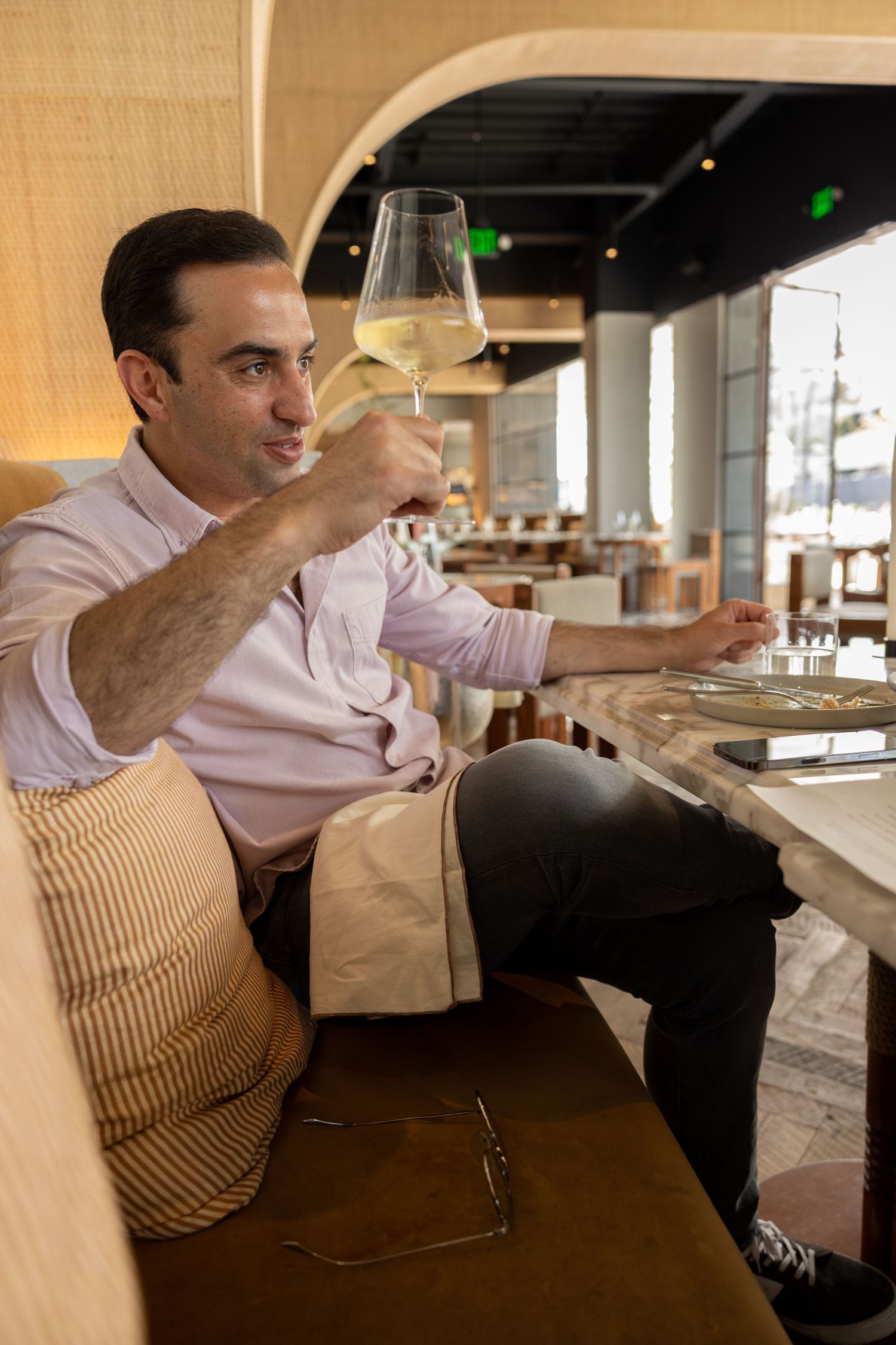 Lifestyle portrait of a man doing a toast while holding a glass of wine in a beautiful, neutral toned modern restaurant.