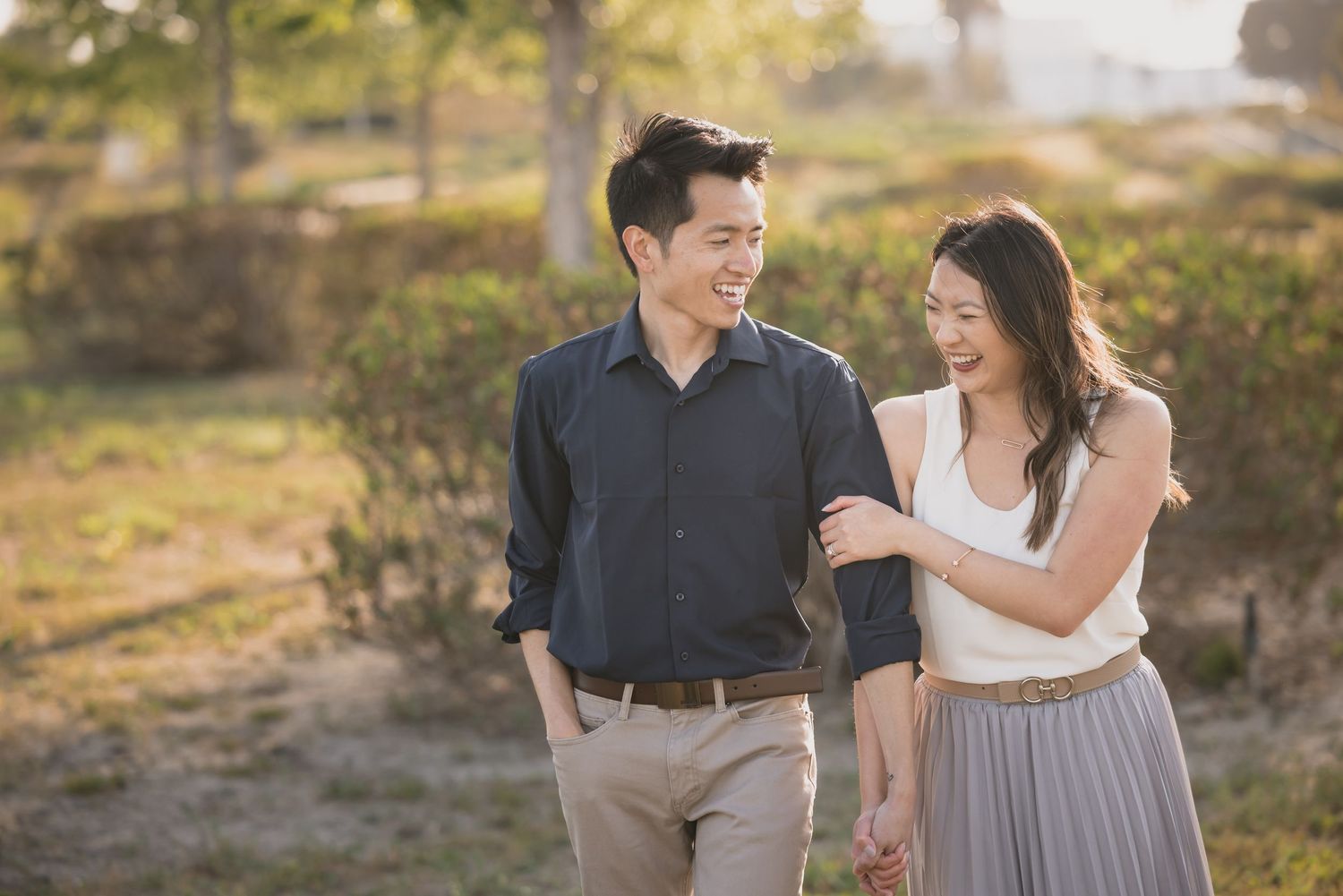 A couple shares a romantic moment while walking in a sunlit outdoor setting.