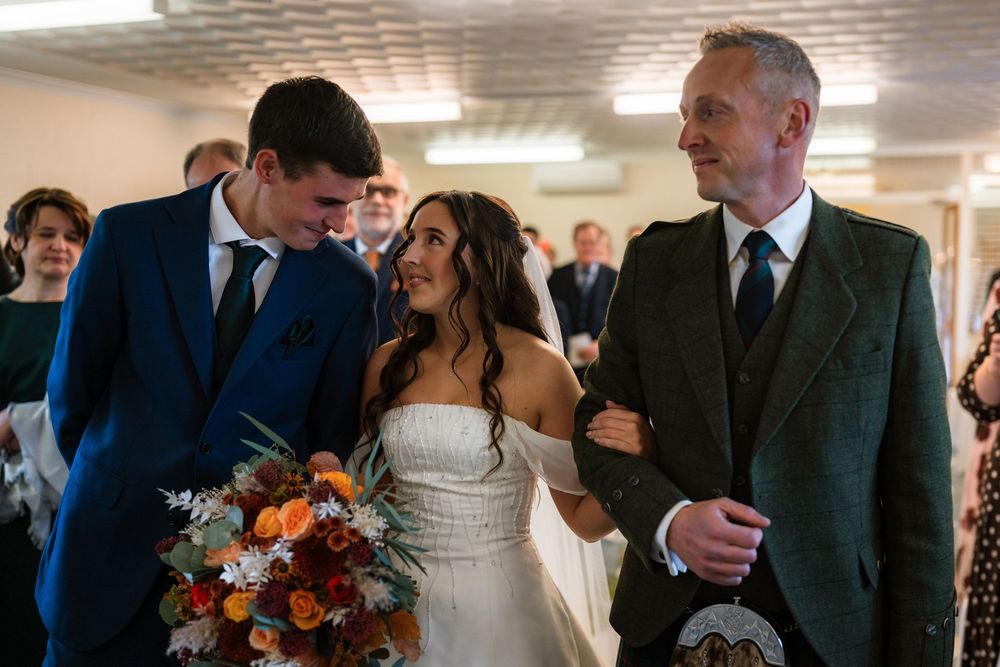 Wedding guests gather in a reception hall with warm lighting and elegant decor.