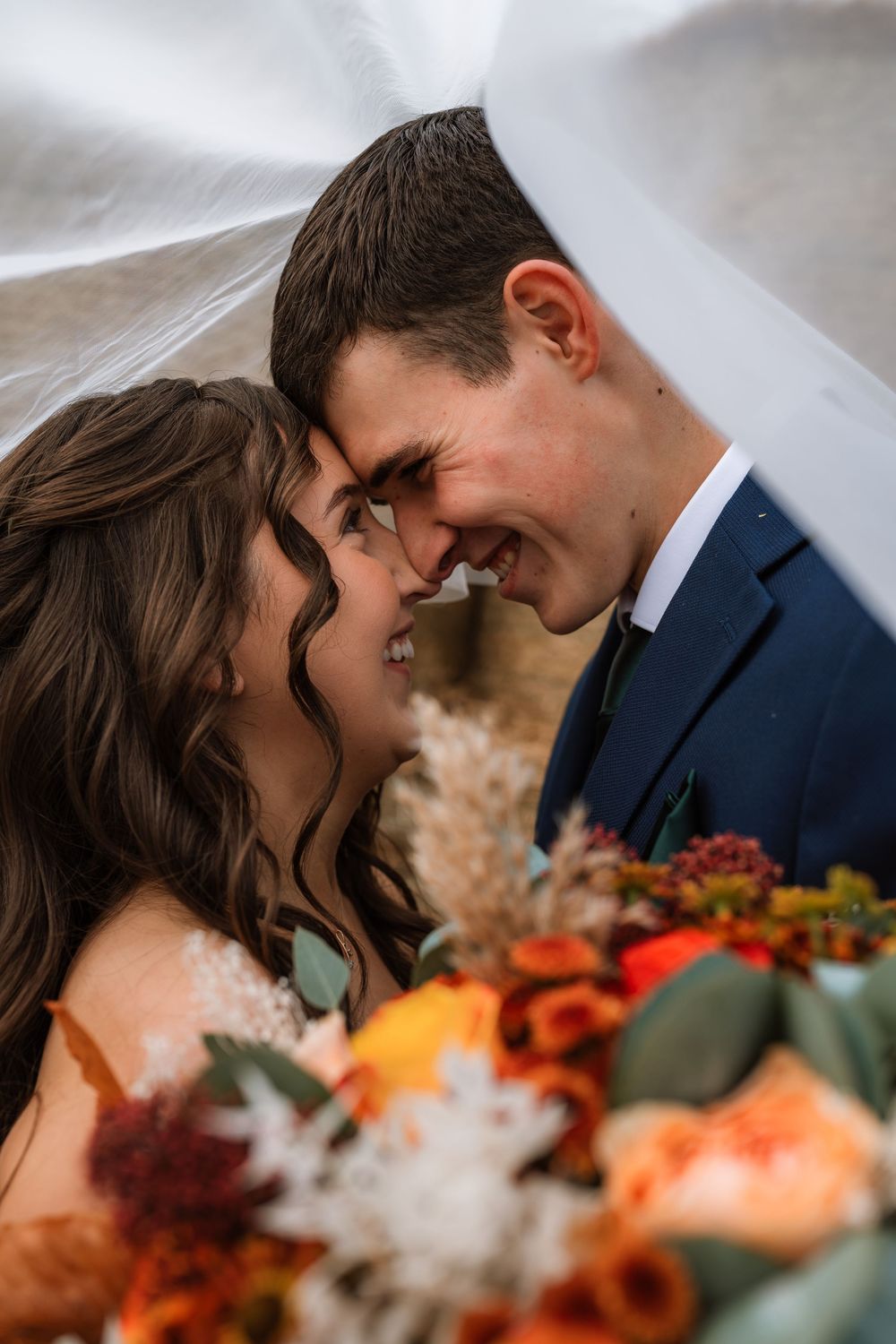 A romantic wedding couple shares an intimate moment together with orange and red autumn florals in the foreground.